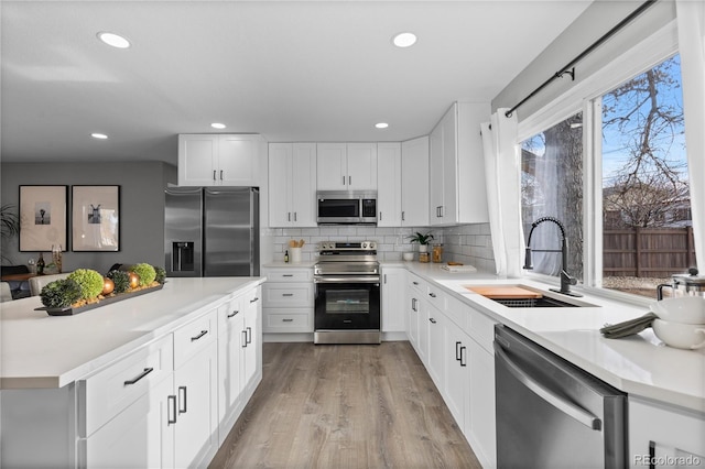 kitchen featuring tasteful backsplash, white cabinetry, sink, stainless steel appliances, and light wood-type flooring