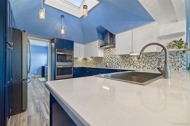 kitchen with white cabinetry, blue cabinetry, wall chimney exhaust hood, and pendant lighting