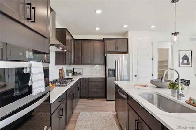 2515 Clayton Cir, Superior, CO 80027 - kitchen featuring stainless steel appliances, wall chimney range hood, dark brown cabinetry, light wood finished floors, and pendant lighting