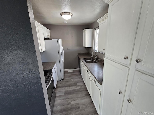 kitchen with dark countertops, white cabinets, wood finished floors, and a sink