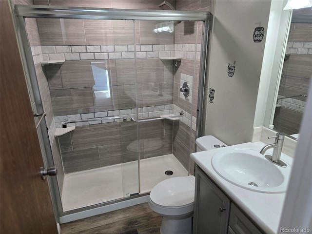 bathroom featuring a shower stall, toilet, vanity, and wood finished floors