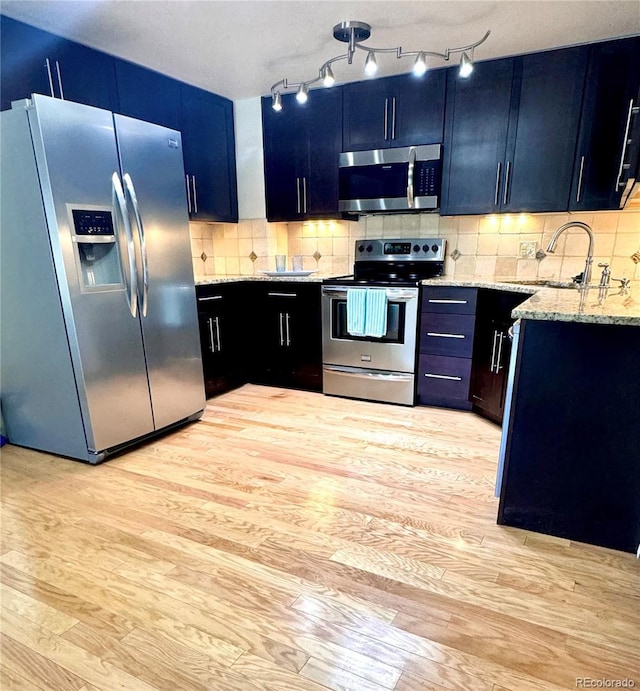 kitchen featuring light stone countertops, light wood-style flooring, stainless steel appliances, and a sink