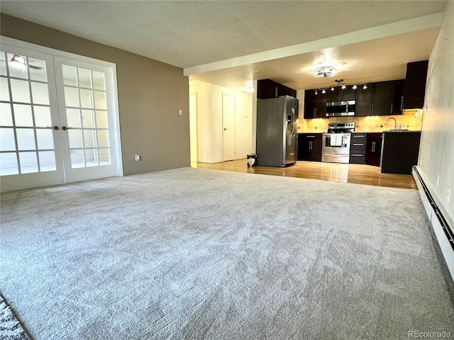 unfurnished living room with french doors, a baseboard radiator, a sink, and light colored carpet