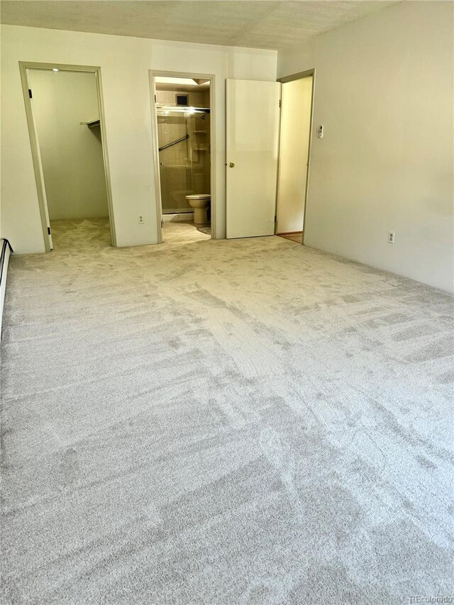 unfurnished bedroom with light colored carpet, ensuite bath, and a spacious closet