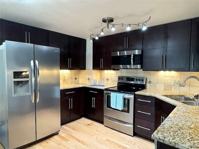 kitchen with stainless steel appliances, a sink, light wood-style flooring, and light stone countertops