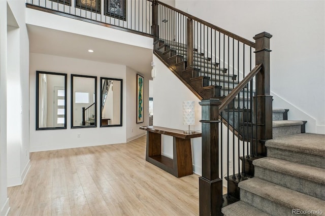 stairs with recessed lighting, a high ceiling, baseboards, and wood finished floors