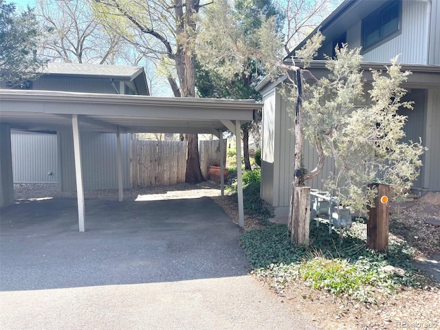 view of vehicle parking featuring driveway, fence, and a carport
