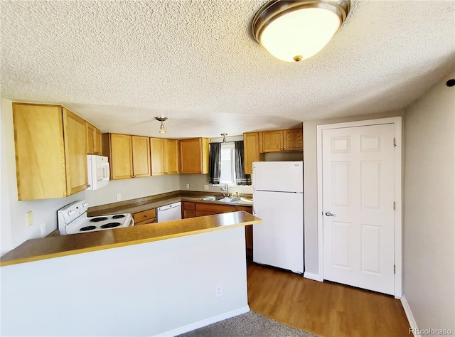 kitchen with a sink, white appliances, a textured ceiling, and a peninsula