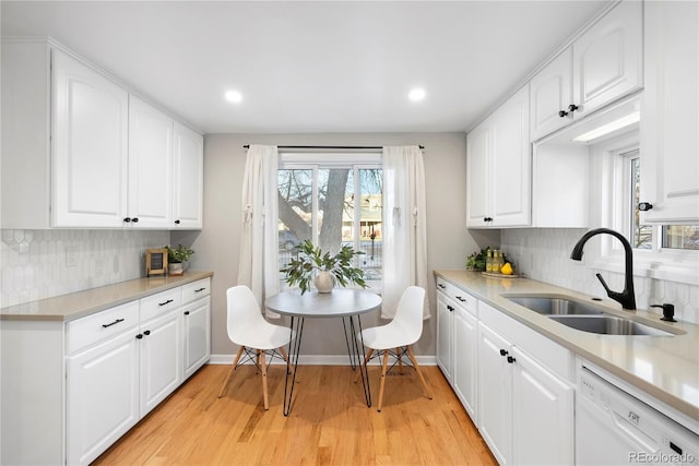 kitchen with backsplash, white dishwasher, sink, light hardwood / wood-style flooring, and white cabinets