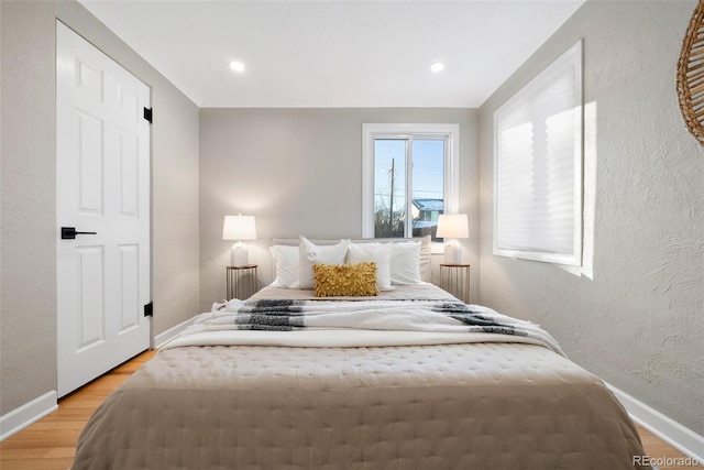 bedroom with light wood finished floors, recessed lighting, baseboards, and a textured wall