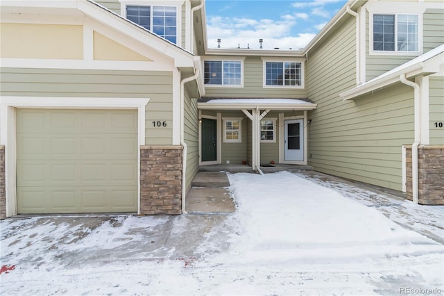 snow covered property entrance featuring a garage and stone siding