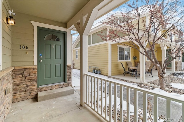 snow covered property entrance with covered porch and stone siding