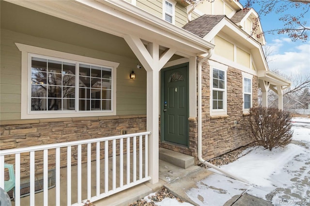 snow covered property entrance with stone siding and roof with shingles