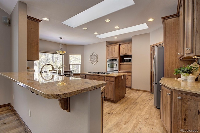 kitchen featuring light wood finished floors, a breakfast bar area, a peninsula, a skylight, and stainless steel appliances