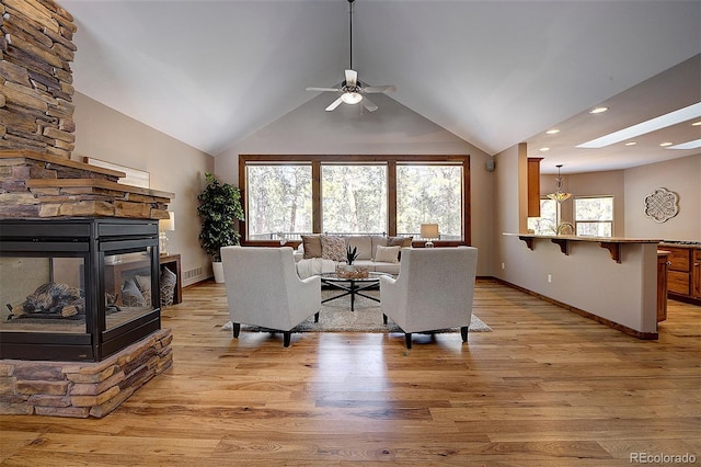 living room with a stone fireplace, light wood-style floors, a ceiling fan, and vaulted ceiling