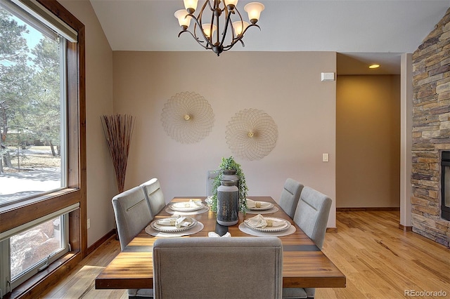 dining space featuring baseboards, lofted ceiling, light wood-style flooring, a stone fireplace, and a notable chandelier