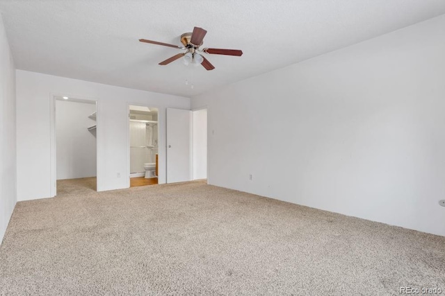 unfurnished bedroom featuring carpet flooring, a spacious closet, ceiling fan, and ensuite bathroom