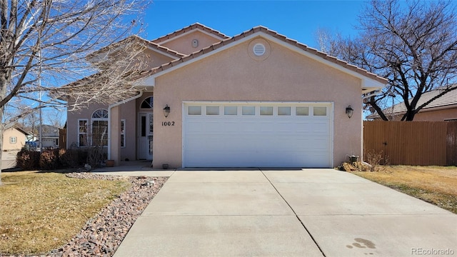 view of front of property featuring a garage, a tile roof, fence, stucco siding, and driveway
