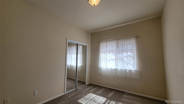 unfurnished bedroom featuring a closet, a textured wall, baseboards, and carpet