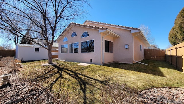 rear view of property featuring a yard, stucco siding, a fenced backyard, and an outbuilding