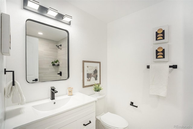 bathroom with a tile shower, vanity, and toilet