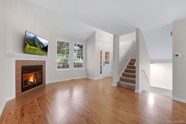 unfurnished living room featuring baseboards, a tiled fireplace, stairway, and wood finished floors