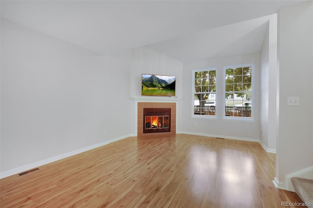 unfurnished living room featuring light wood-type flooring, a tiled fireplace, visible vents, and baseboards