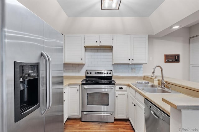 kitchen with stainless steel appliances, a peninsula, a sink, light countertops, and decorative backsplash