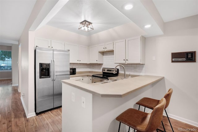 kitchen with appliances with stainless steel finishes, a peninsula, a kitchen breakfast bar, and tasteful backsplash