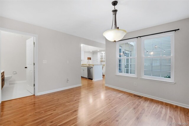 unfurnished living room featuring visible vents, a sink, light wood-style flooring, and baseboards