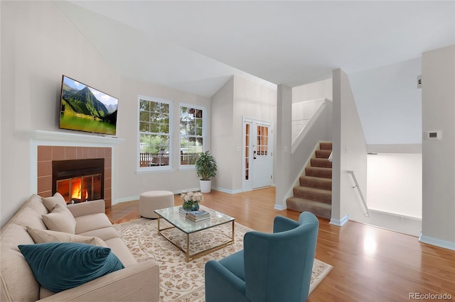 living area featuring stairs, baseboards, wood finished floors, and a tiled fireplace