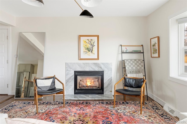 sitting room with a premium fireplace, wood finished floors, visible vents, and baseboards