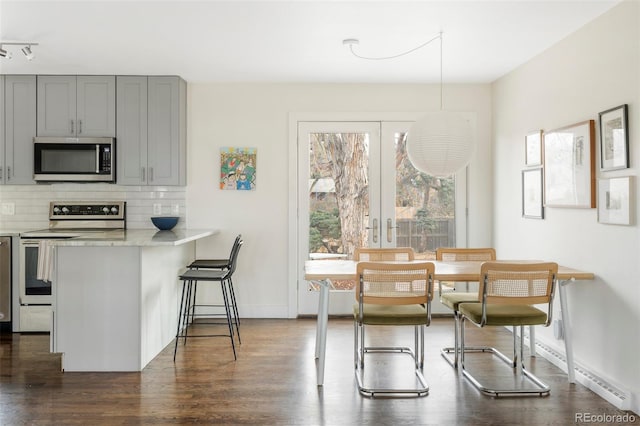 kitchen featuring dark wood-style floors, light countertops, decorative backsplash, gray cabinetry, and appliances with stainless steel finishes