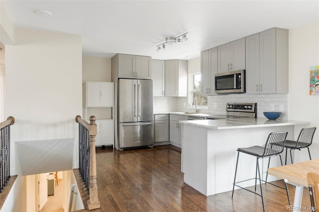 kitchen featuring tasteful backsplash, dark wood finished floors, appliances with stainless steel finishes, a peninsula, and gray cabinetry