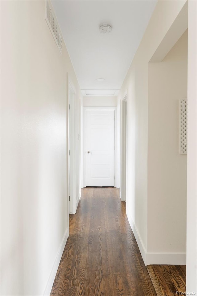 hall with dark wood-style flooring, visible vents, and baseboards