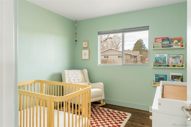 bedroom featuring a crib, baseboards, and wood finished floors