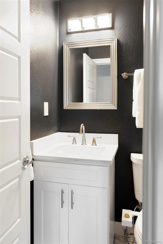 bathroom featuring a textured wall, vanity, and toilet