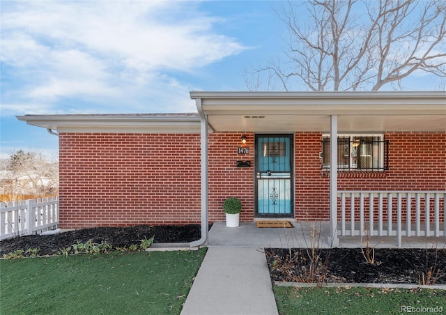 doorway to property with covered porch, fence, and brick siding