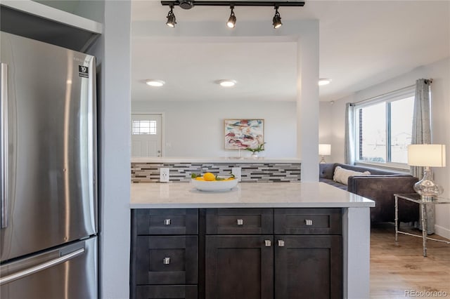 kitchen featuring light wood-type flooring, light stone counters, backsplash, freestanding refrigerator, and a peninsula