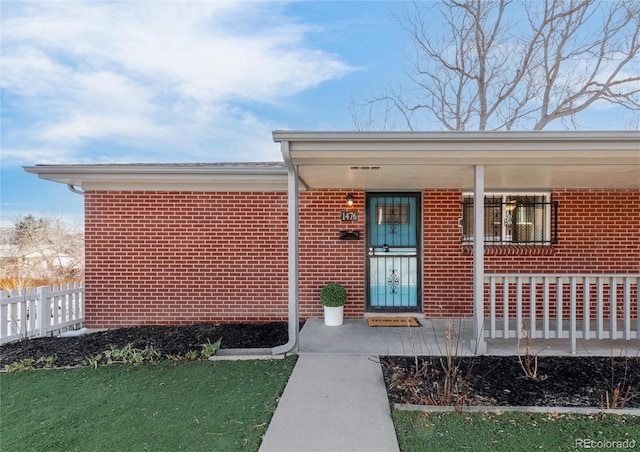 doorway to property with a porch, fence, and brick siding