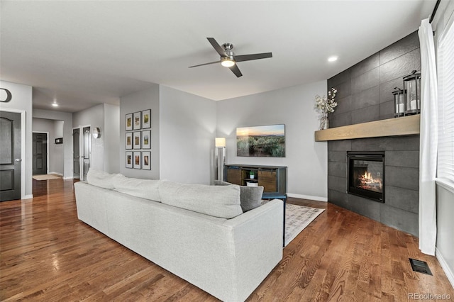 living room featuring dark wood finished floors, a tile fireplace, visible vents, and baseboards