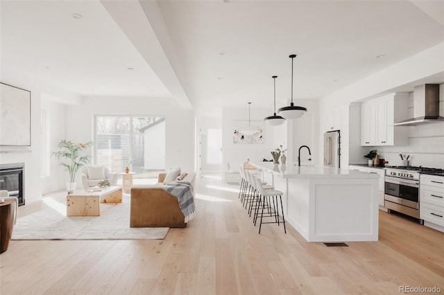 kitchen featuring high quality appliances, open floor plan, wall chimney exhaust hood, light wood finished floors, and decorative backsplash