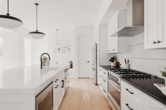 kitchen featuring a sink, appliances with stainless steel finishes, white cabinets, and wall chimney range hood