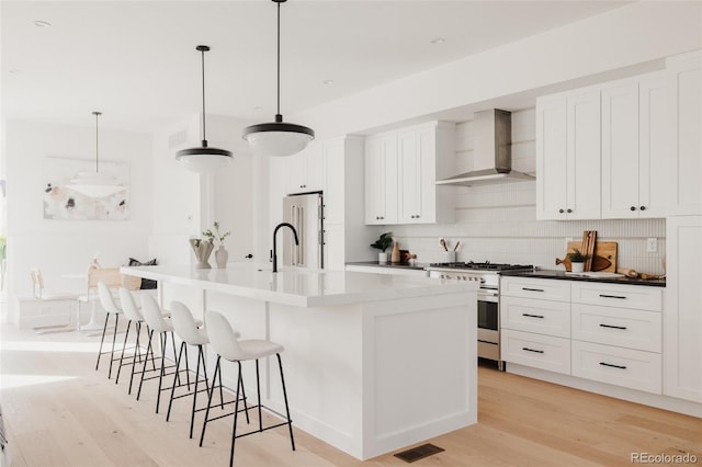 kitchen featuring visible vents, high quality appliances, wall chimney exhaust hood, and light wood-type flooring