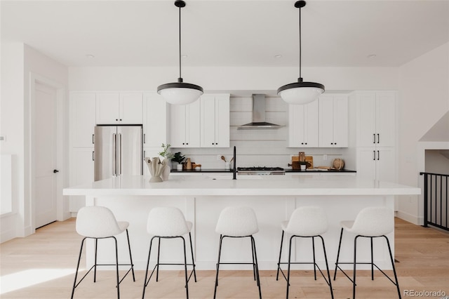 kitchen featuring high end fridge, tasteful backsplash, light wood-style floors, white cabinets, and wall chimney range hood