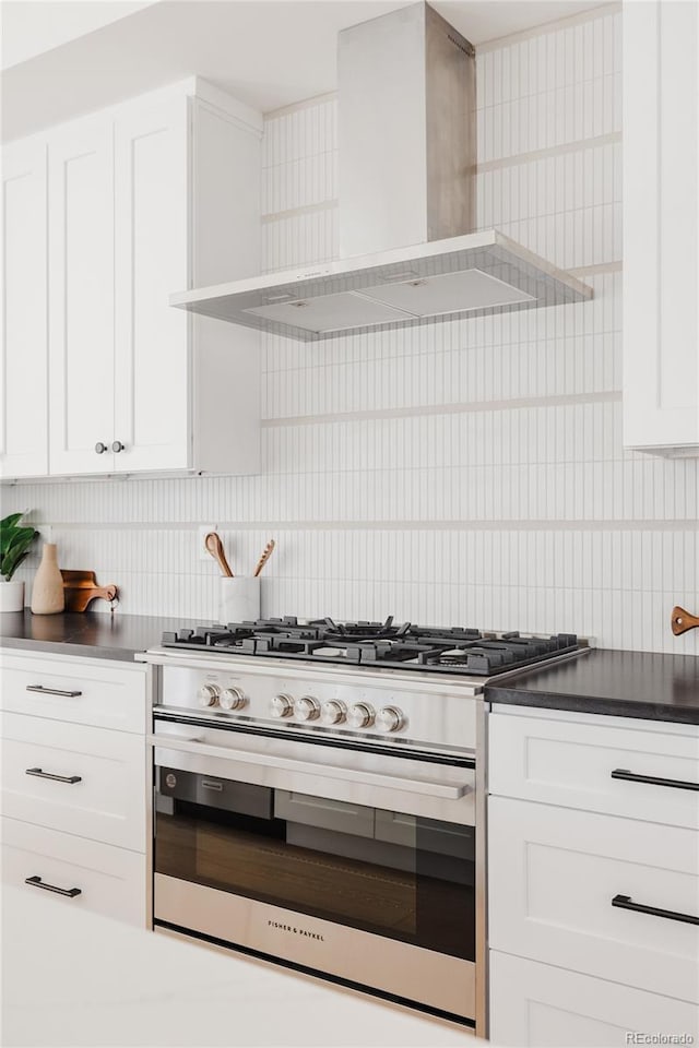 kitchen featuring tasteful backsplash, dark countertops, wall chimney range hood, white cabinets, and stainless steel gas range