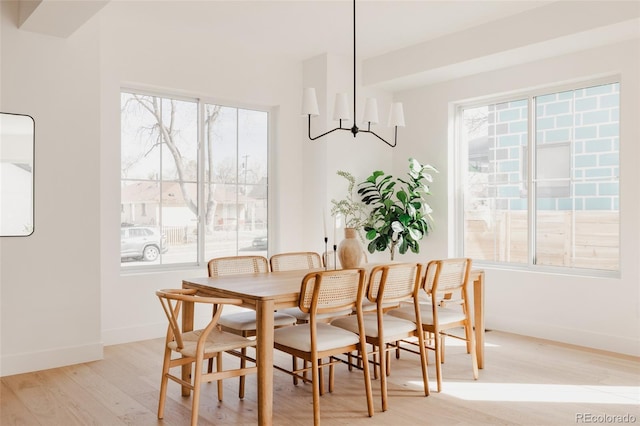 dining space featuring a healthy amount of sunlight, baseboards, light wood finished floors, and a chandelier