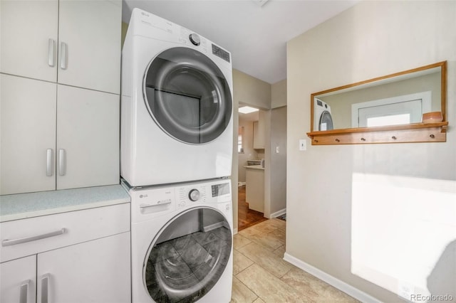 washroom featuring stacked washer and dryer, baseboards, and cabinet space
