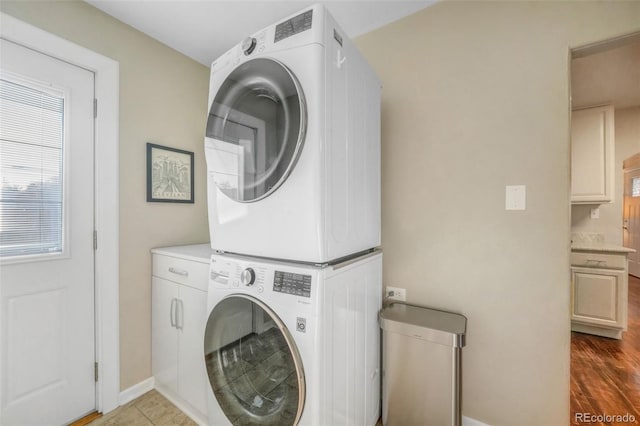 clothes washing area with stacked washing maching and dryer, baseboards, and cabinet space