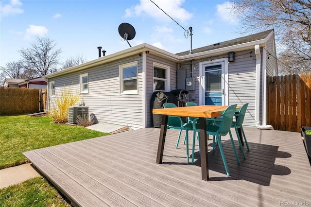 deck featuring outdoor dining space, central AC unit, fence, and a lawn